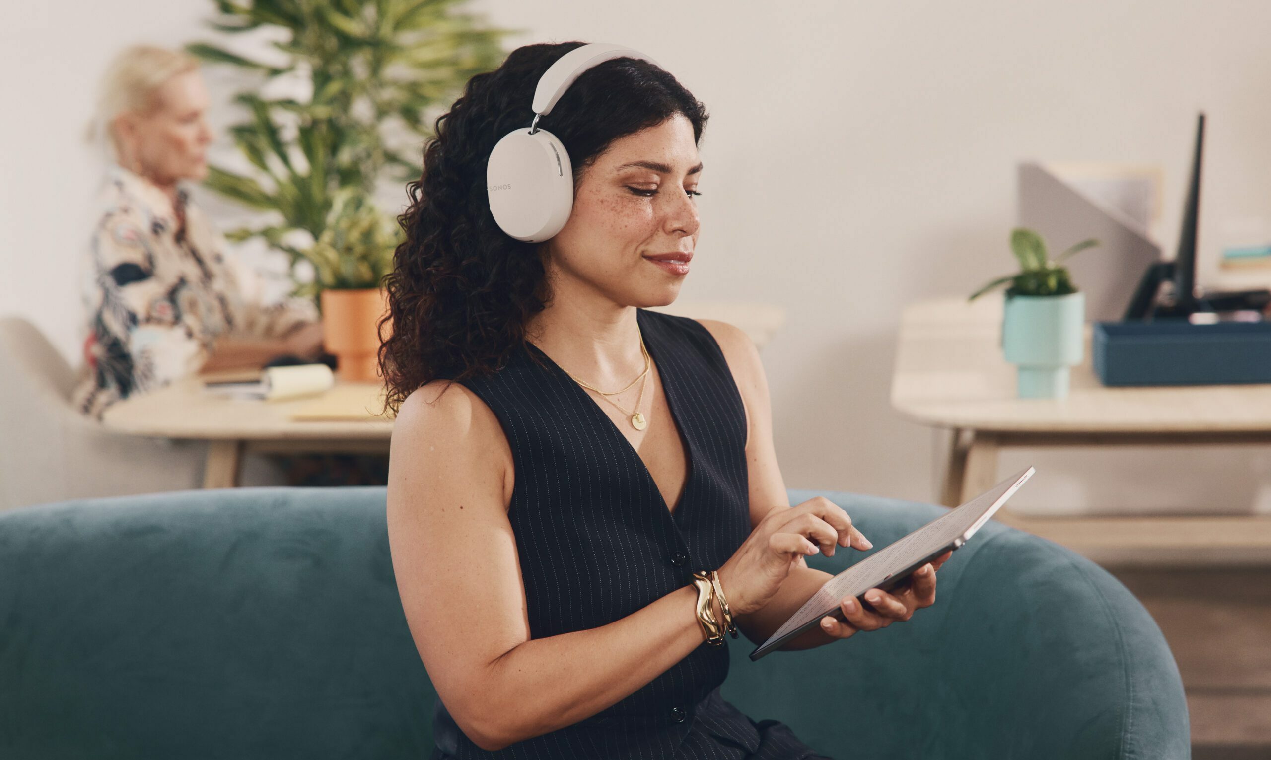 Femme dans un salon, avec sur les oreilles le tout nouveau Sonos Ace