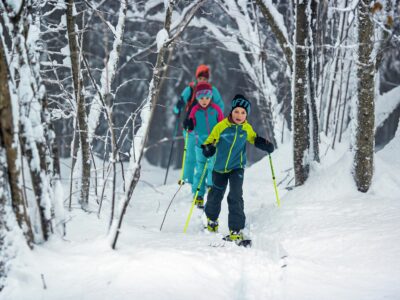 Famille dans la neige en skis de randonnée, équipée du pack youngstar